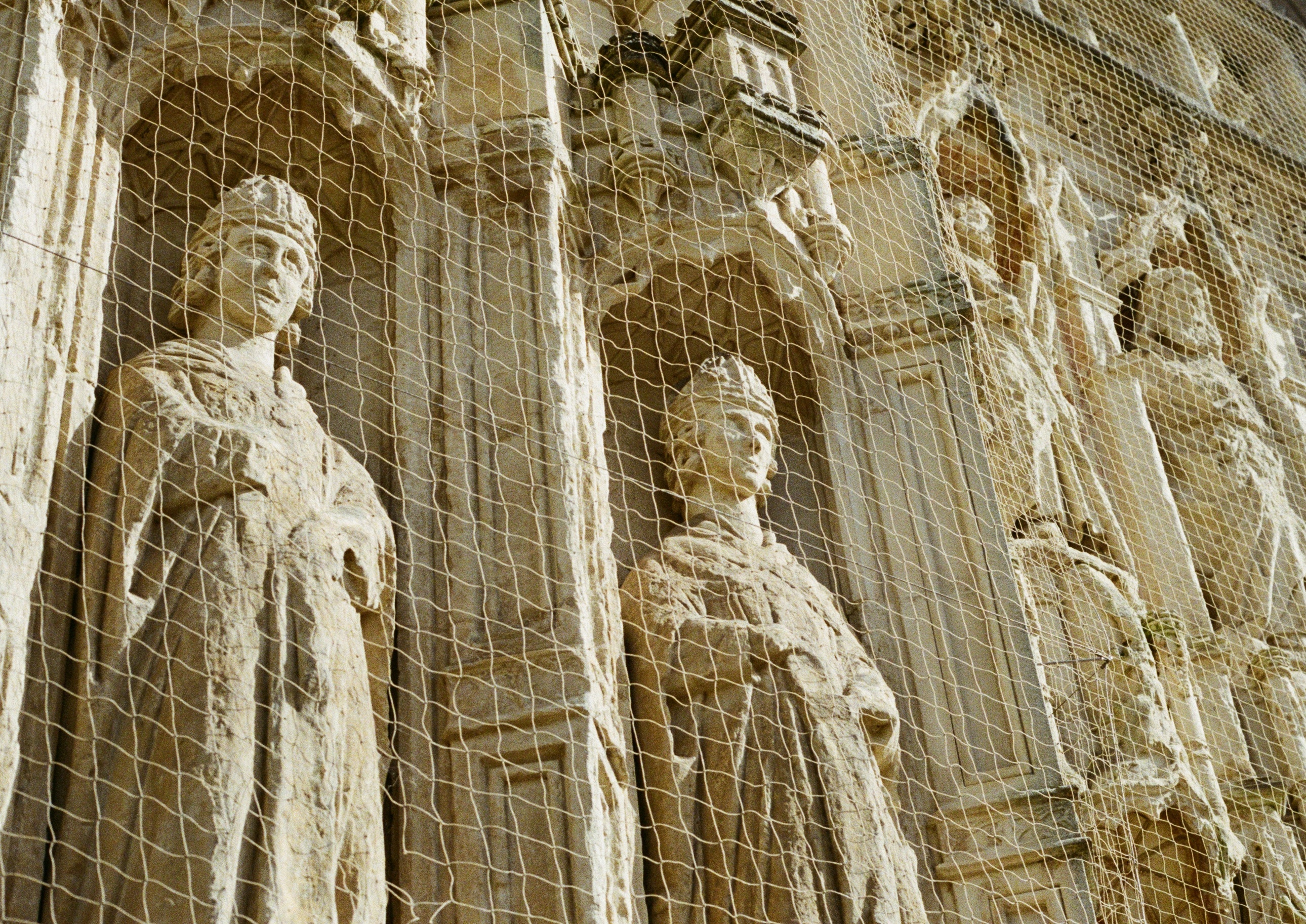 weathered stone statues of bishops behind protective netting
